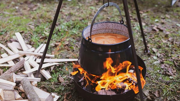 Soup cooking in a pot above an open fire outdoors.